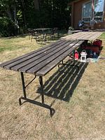 Photo showing two long folding tables with wood plank tops and black metal bases on grass outdoors.