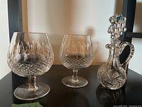 Two Waterford brandy glasses and one Marquis crystal decanter with stopper arranged on a black shelf, showing the cut patterns and overall shapes.
