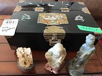 Black Asian jewelry box with three carved stone figurines displayed in front, showing details and size relation.