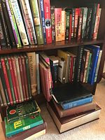 Books on shelf and stacked including fiction and non-fiction titles such as 'Pol Martin', 'The Ship's Medicine', 'Household Tips' and 'James Patterson' among others