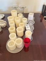 Glass candle holders and multiple ivory pillar candles, some round and some square, along with a red glass candle.