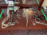 Full lot showing assortment of costume jewelry including necklaces, bracelets, earrings, rings, keychain, and jewelry box on wooden surface.