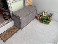 Overview photo showing plastic deck box, garden mat, garden ornaments, and gloves on porch floor.