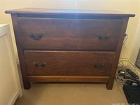 Front view of wood two drawer dresser with metal pull handles showing drawer fronts and overall condition.