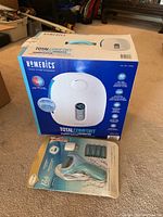 Box of Homedics Total Comfort ultrasonic humidifier with product image and features on the front, placed on carpet floor with Pediperfect foot file package in front