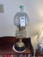 Full view of the glass oil lamp showing the textured transparent glass font and chimney, brass burner, terra cotta section, and wooden base sitting on a wooden surface.