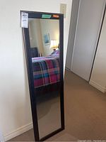 Full view of the tall rectangular wall mirror leaning against a wall in a bedroom showing its size and reflection.
