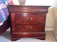 Wooden night stand shown with two drawers and metal handles, positioned beside bed.