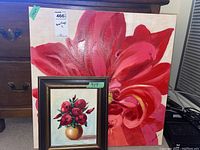 Photo showing both paintings: a small framed floral still life and a large unframed red flower painting