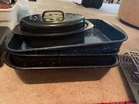 Stack of three black speckled roasting pans, including one with lid and handles