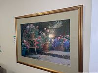 Framed floral print by Allan Mynozak hanging on a wall, showing a garden patio scene with flowers and a lamp.