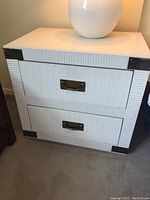 Front angled view of white painted side table showing 2 drawers with metal handles and rattan texture detailing on drawer fronts and corners