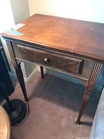 Front angle view of vintage wood side table showing drawer and leg details with some scratches on top surface.