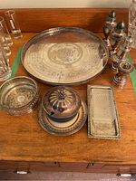 Set of silver plated serving trays and tableware including round footed serving tray with engraved pattern, rectangular serving tray, primrose plate bottle coaster, silver plate and china lidded bowl, salt and pepper shakers, and candlesticks.