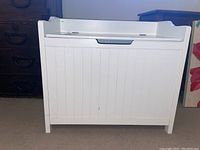 Photo showing front view of white wooden storage bench with hinged lid and paneled front design.