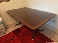 Wooden dining room table fully extended with two 15-inch extensions, showing dark wood with lighter trim and pedestal legs with brass caps.