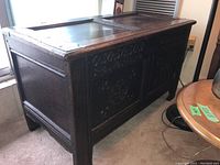 Front and side view of antique wooden trunk showing carved detailing and hinged lid.