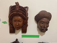 Two Asian wood carved masks hanging on wall, one female and one male