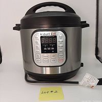 Front view of the Instant Pot electric pressure cooker. The control panel is visible, showing various cooking option buttons and a digital display. The cooker has a handle on top and side handles.
