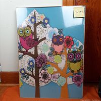 Front view of Ikea Solmyra framed print featuring colorful owls and floral trees in blue background, sealed in original shrink wrap.