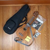 Photo showing entire Kmise ukulele starter set including ukulele, carrying bag, strap, tuner, tuning fork, quick start guide, and small parts bag on wood floor.