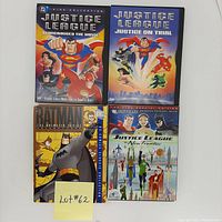 Photo showing four superhero animated DVDs including Batman The Animated Series Volume 4 and three Justice League DVDs: Starcrossed The Movie, Justice On Trial, and The New Frontier, arranged on a white surface with a handwritten lot number.