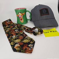 Photo of three Disney collectible items on white background: grey ball cap with Mickey patch, green Tigger mug with 3D face, and black Seven Dwarfs tie with colorful print.