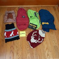 Six extra small dog coats and sweaters laid out on wooden floor, showing range of colors and styles including sweaters and coats.