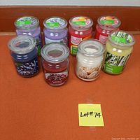 Photo of 8 jar candles with different colored waxes and scented labels on an orange surface.