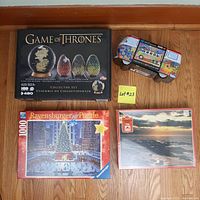 Four jigsaw puzzle boxes arranged on a wooden floor: Game of Thrones Collector Set (480 pieces), Volkswagen Bus Puzzle (550 pieces), Canadian Guild Puzzle (750 pieces), Ravensburger Christmas Puzzle (1000 pieces). A post-it with 'Lot #23' is present.