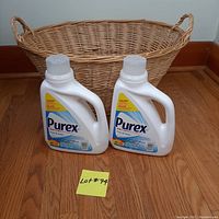 Wicker laundry basket with two bottles of Purex Free and Clear laundry detergent in front of it, placed on hardwood floor.