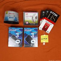 Clear overview of all items in the lot showing Maxell DVD-R spindle, Staples DVD+RW pack, TDK VHS tapes, and 3-packs of disc storage cases.