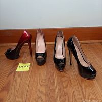 Pair of women's high heel shoes size 8, one black patent leather peep toe platform heel, one red to black gradient patent leather peep toe platform heel, displayed side by side on wooden floor.