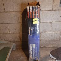 Mastercraft folding work bench box standing upright against a concrete wall, showing front of the packaging with product images and branding.