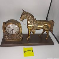 Front angle of vintage brass finished Western horse electric mantle clock with horseshoe-shaped clock face and mounted on rectangular base.