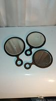 Three antique wood hand mirrors with black wooden frames and handles, beveled edges, graduated sizes, placed reflective side up on a white surface.