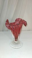 Front angle view of cranberry glass vase with ruffled top and clear base on a neutral background.