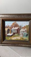 Framed miniature oil painting showing several houses in a rural landscape with autumn trees and birds in the sky.
