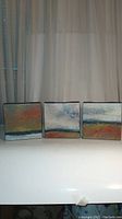 Triptych set of three small, square, gallery wrapped canvases with textured modern abstract art on display together.
