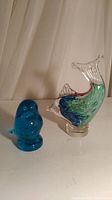 Both glass animal figurines displayed side by side on a white surface with neutral background, showing size and color contrast.