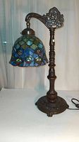 Full view of the Tiffany style lamp showing the stained glass shade, ornate bronze metal stand and base.