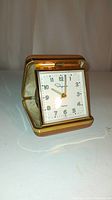 Photo showing the Ingraham folding pocket alarm clock opened and standing, displaying clock face with black Arabic numerals and gold tone hands.