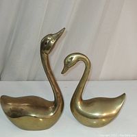 Front view of two brass swan figurines, showing their size and shape differences.