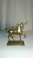 Front view of vintage brass unicorn statue with raised front leg, detailed mane, long horn and medieval gothic-style tail on rectangular base.