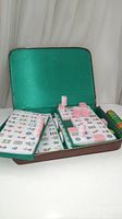 Open vintage mahjong set displayed in green fabric-lined case showing multiple stacks of rectangular pink layered tiles with mattes markings.