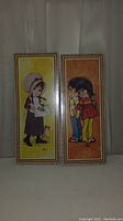 Pair of vintage framed wall art pictures with mod style groovy kids, in original shrinkwraps, shown side by side on a white fabric backdrop.
