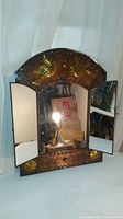 Photo showing vintage tin hanging wall unit with three mirrors open, central doors reveal three mirrors, two on doors and one inside, embossed with bird and flower designs.