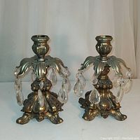 Pair of ornate metal candleholders with seven hanging clear crystal prisms each, shown side by side against a neutral backdrop