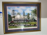 Framed artwork showing a detailed house surrounded by trees, signed print by Larry Anderson, with gold frame and blue matting.