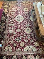 Full view of the burgundy area rug showing intricate floral and geometric patterns with black and cream borders.